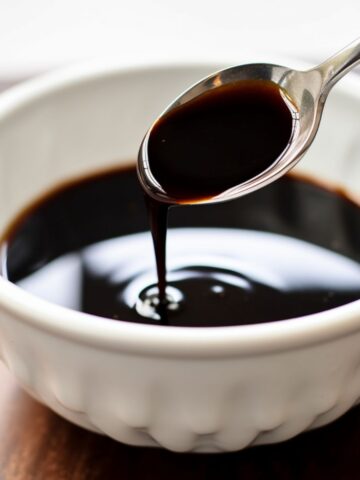 A spoon drizzling balsamic glaze into a small white bowl.