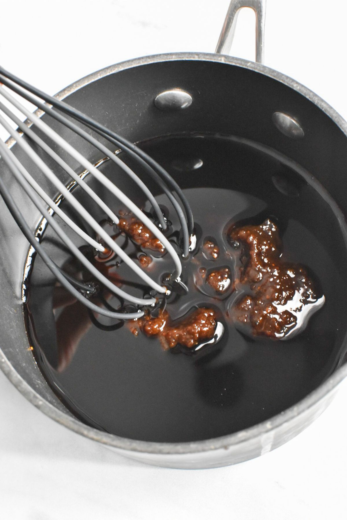 A small saucepan with balsamic vinegar and fig jam with a whisk mixing it together.