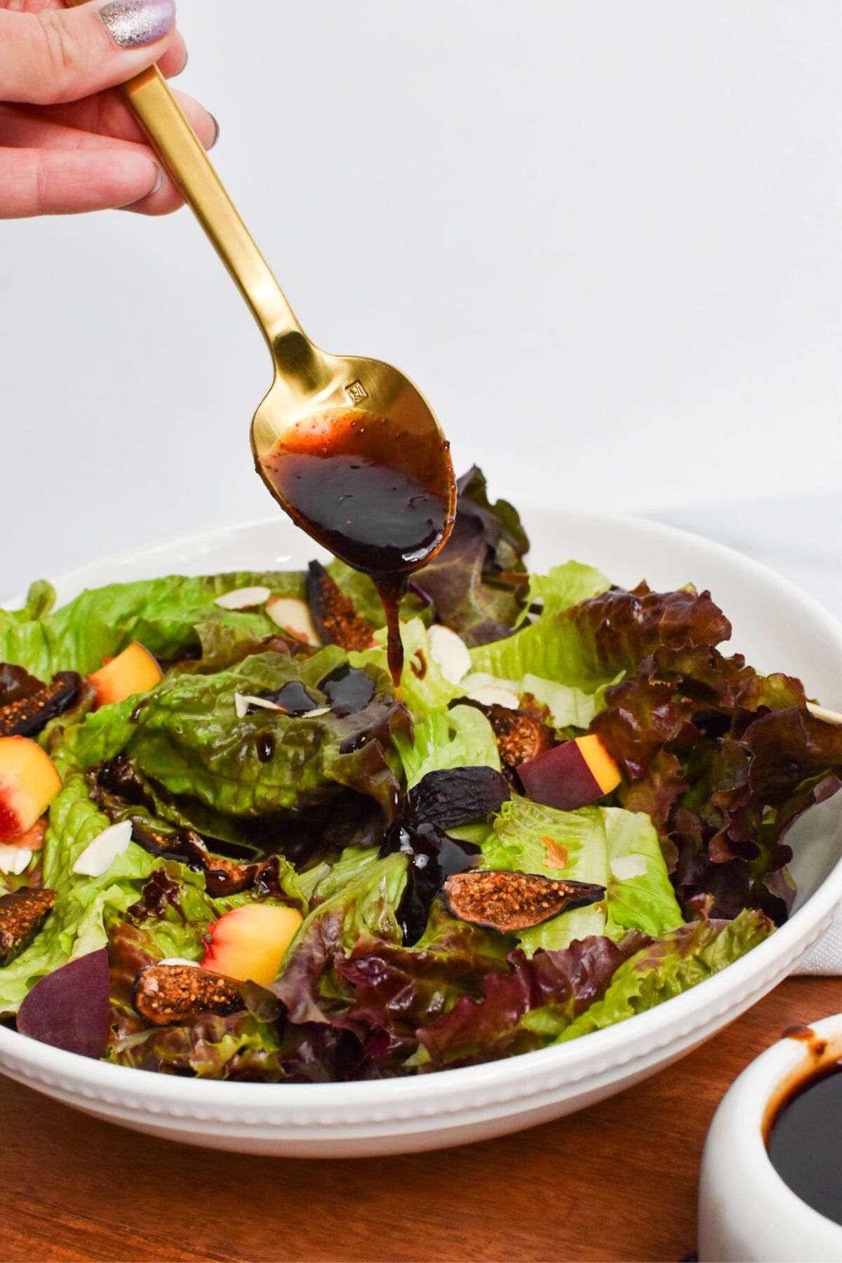 Thick fig glaze being drizzled from a gold spoon onto a salad.