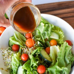 Sweet balsamic vinaigrette being poured over a green salad from a mason jar.