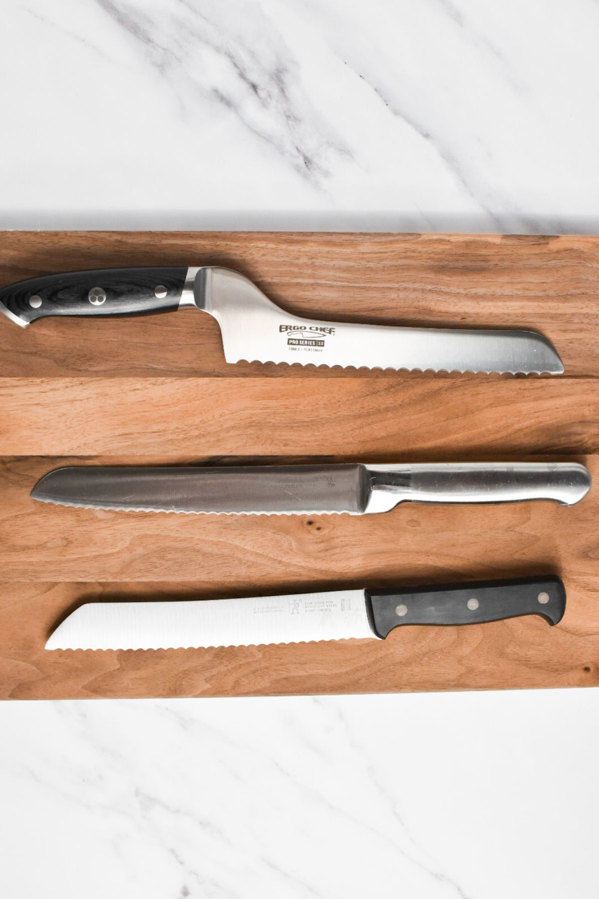 Three serrated bread knives on a wooden cutting board.
