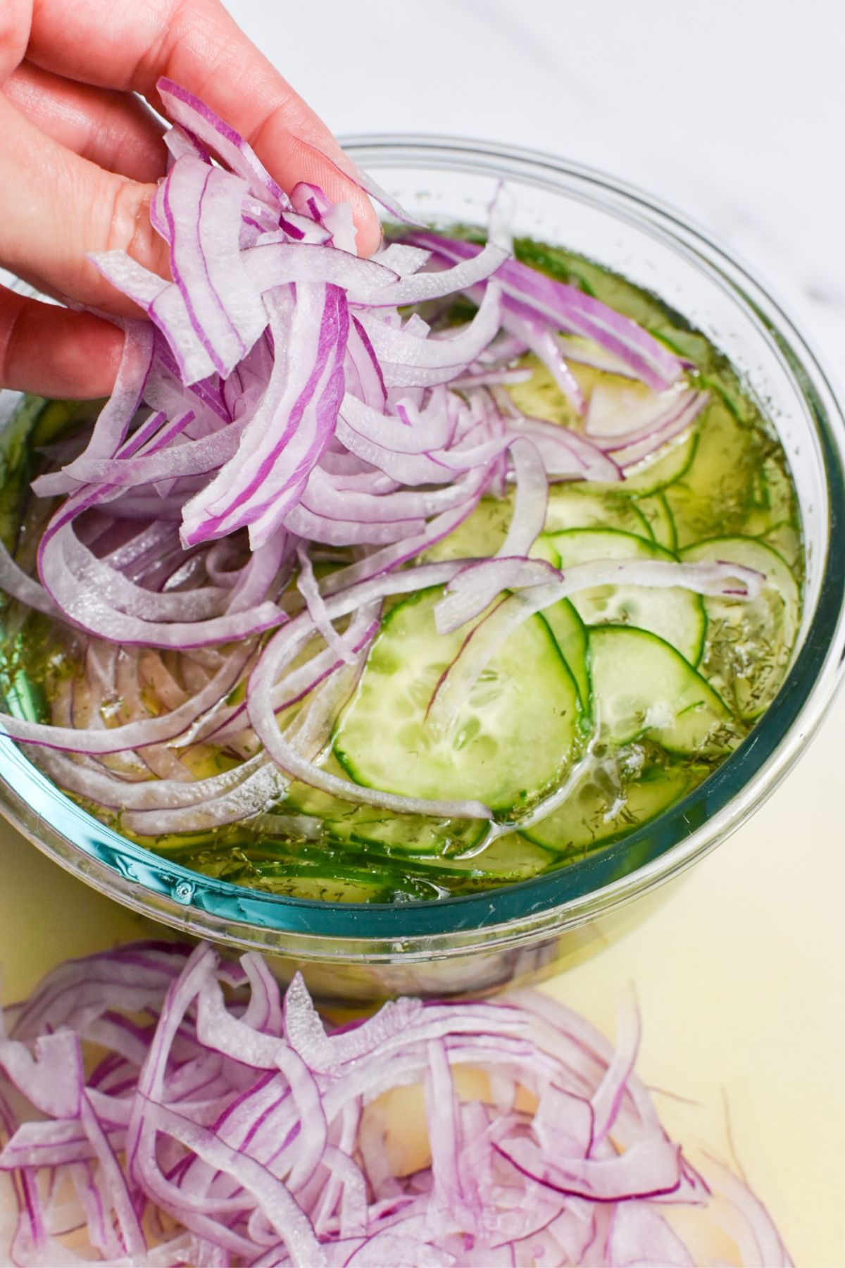 Red onion being added to a bowl of cucumbers, apple cider vinegar and water.