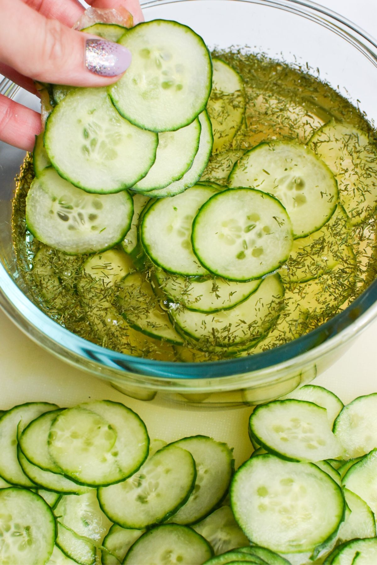 Cucumbers being added to a bowl of apple cider vinegar, water, dill and sugar.