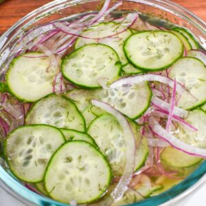 A bowl with cucumbers, onion, apple cider vinegar, sugar and dill.
