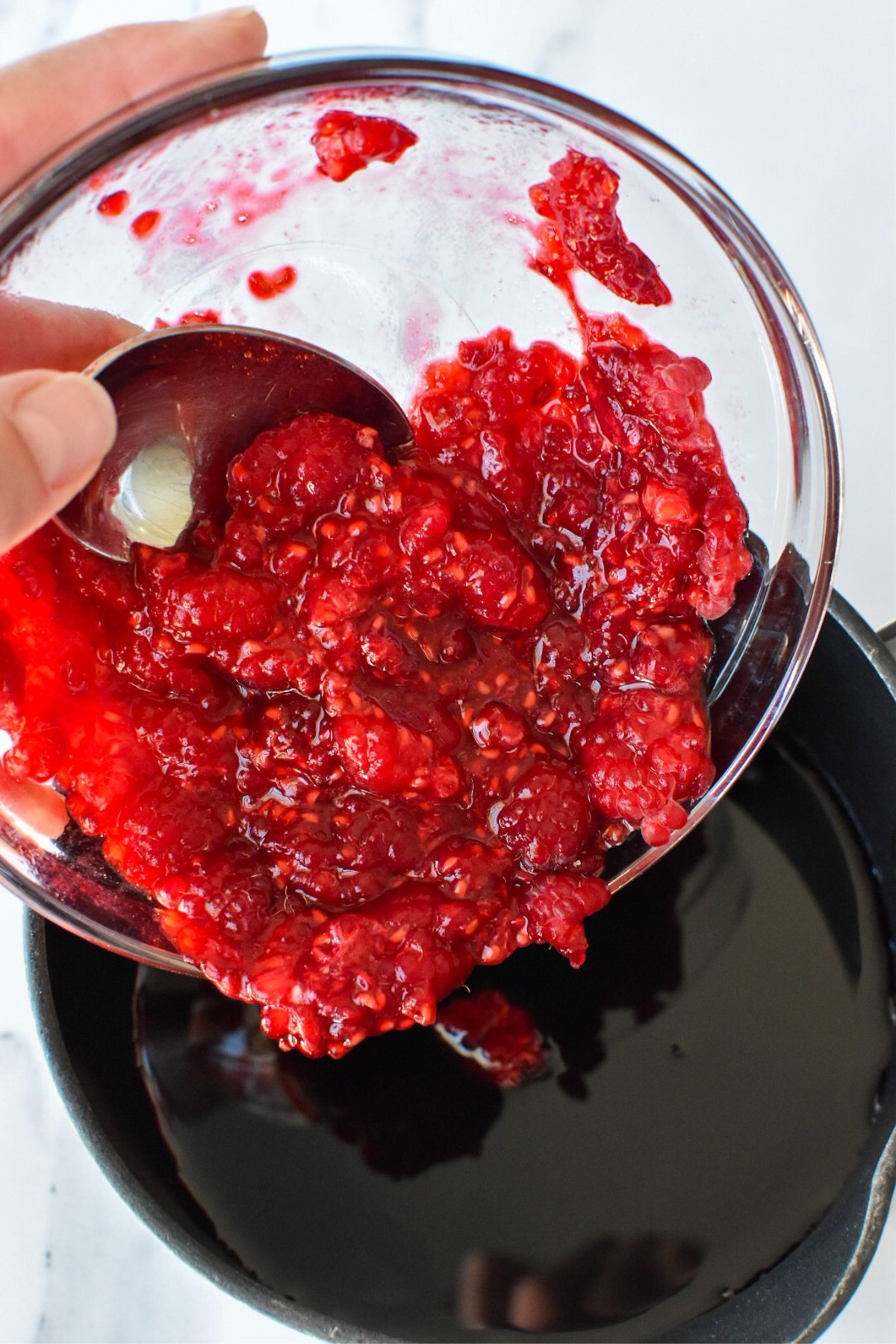 Smashed raspberries are being poured into a small saucepan of balsamic vinegar.