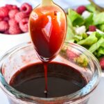 Raspberry balsamic glaze falling from a spoon into a glass bowl.