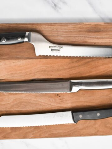Three serrated bread knives on a wooden cutting board.