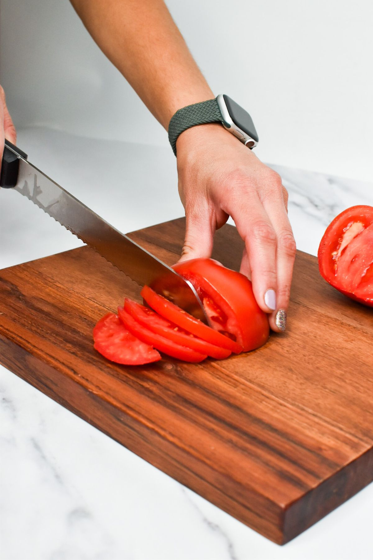 A bread knife being used to cut tomatoes on a wooden cutting board.