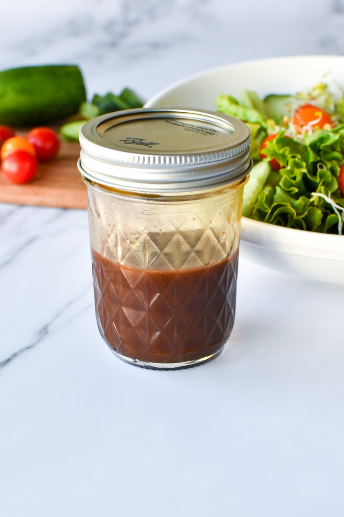 A mason jar of sweet balsamic vinaigrette with a salad in the background.