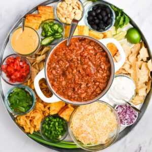 A dutch oven of chili with chili toppings surrounding it.