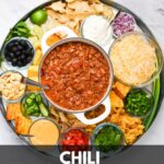 A dutch oven of chili with chili toppings surrounding it and the text: chili charcuterie board.