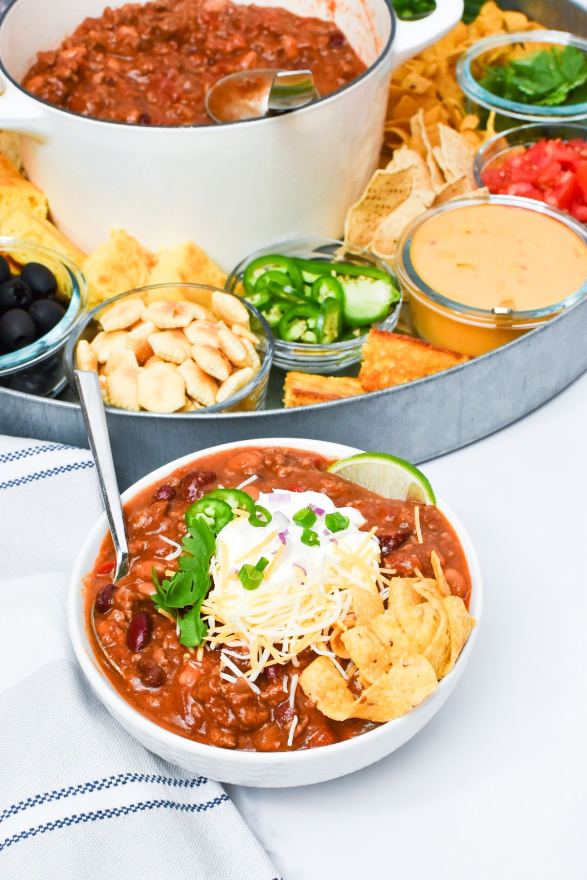A bowl of chili in front of a large selection of chili toppings.
