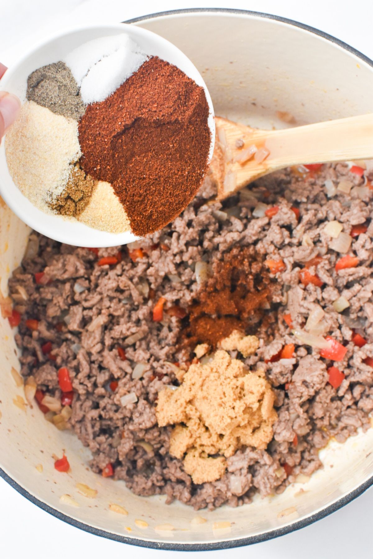 Spices are being added to browned ground beef.