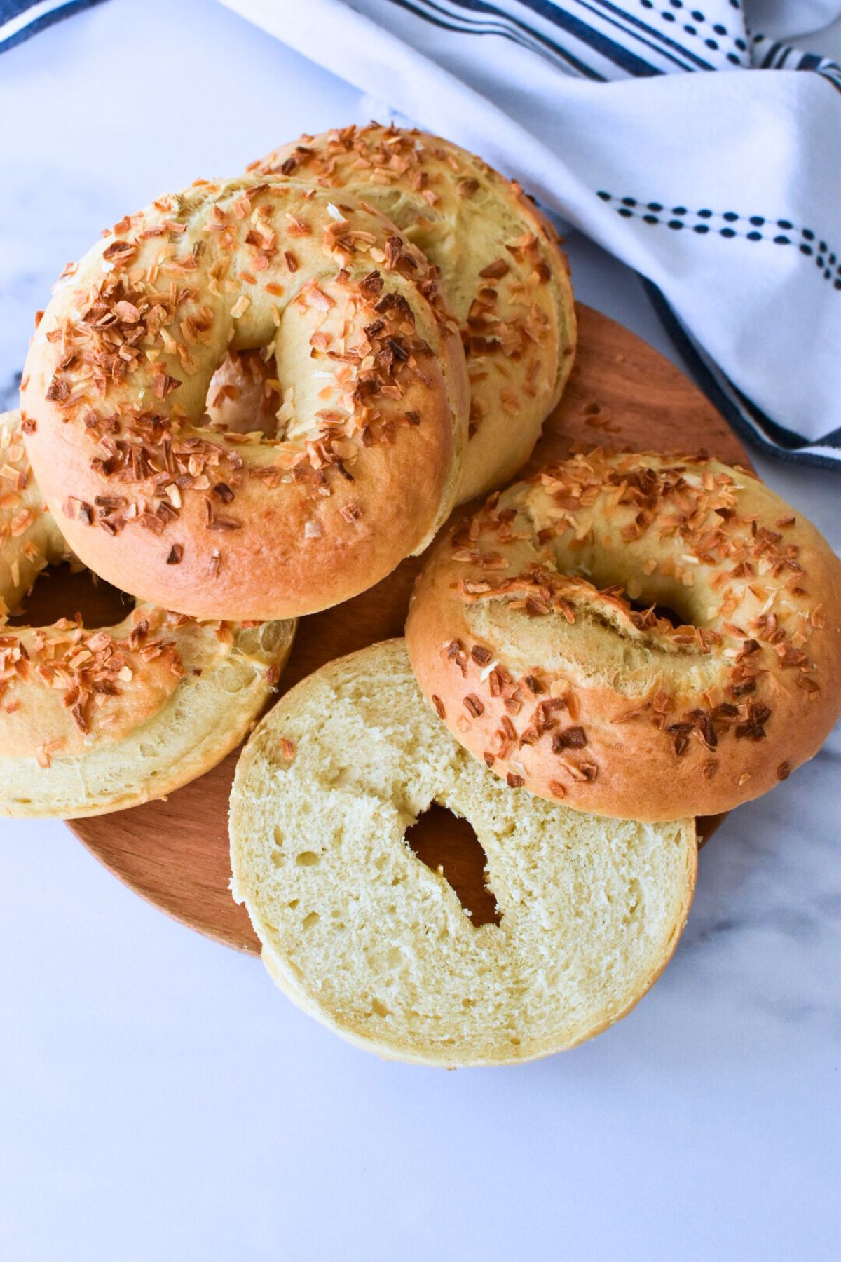 Onion bagels on a wooden plate and one is sliced in half to show the crumb.