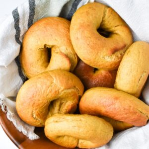 A wooden bowl with a towel in it and pumpkin bagels laying on top.
