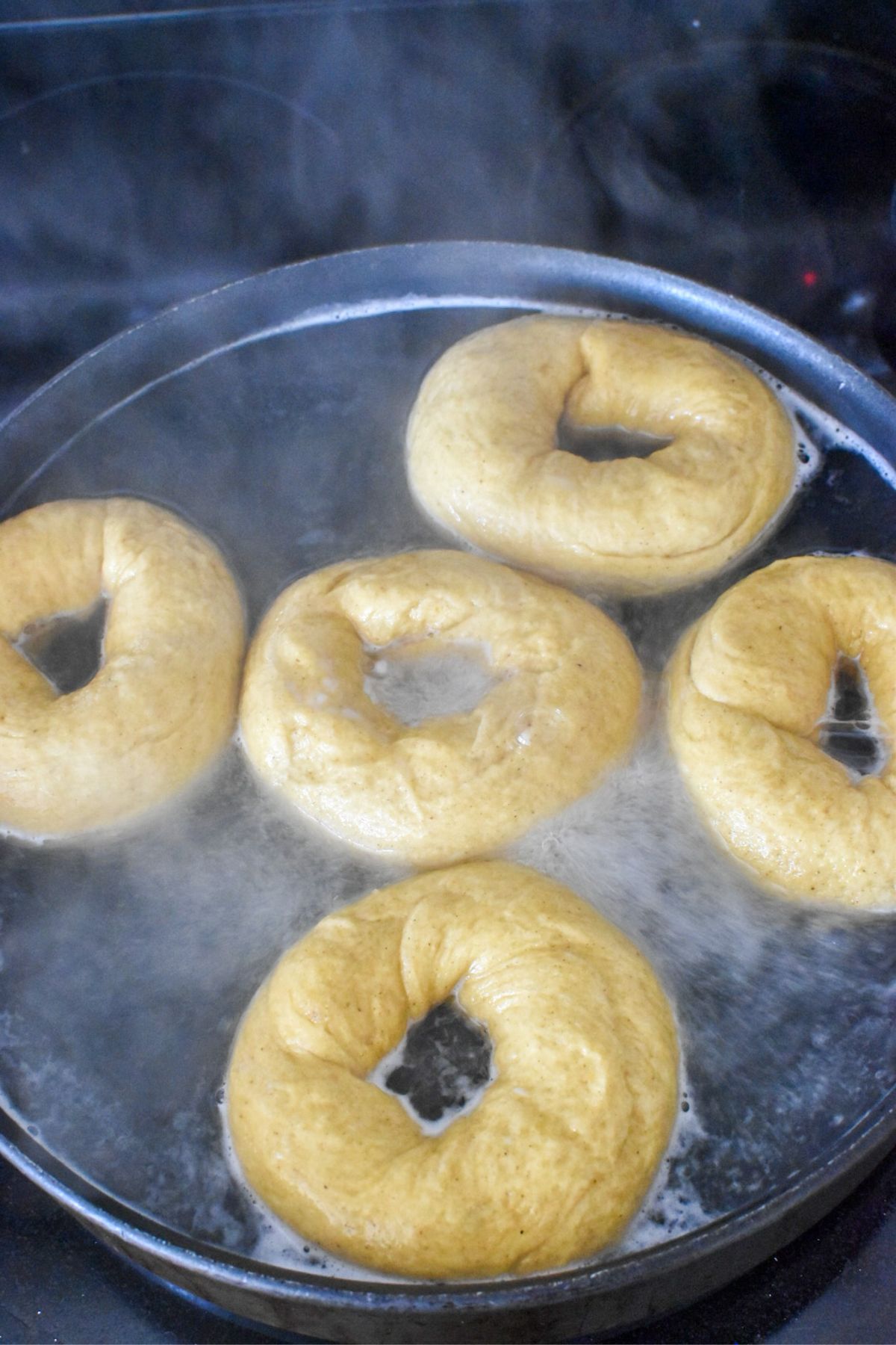 Boiling pumpkin bagels in a large pan on the stove.