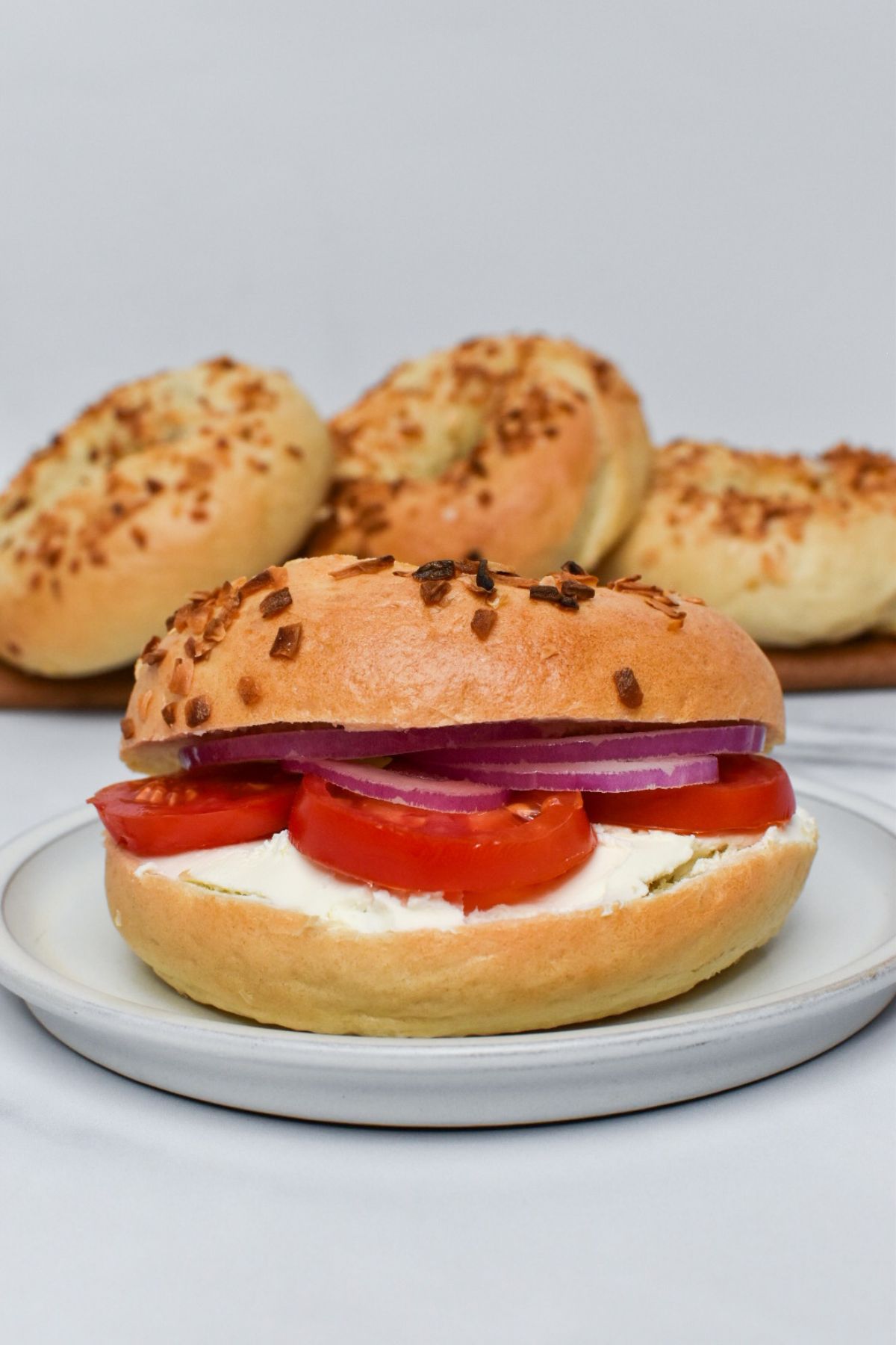 An onion bagel with cream cheese, tomato, and red onion on it with more bagels in the background.