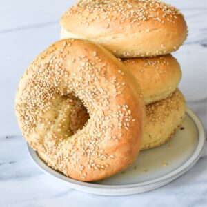 Homemade sesame seed bagels stacked on a plate.