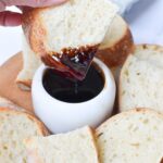 A piece of bread being dipped in a thick balsamic glaze.