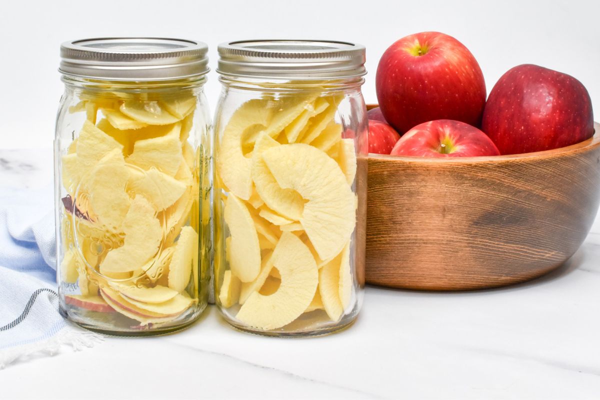 Freeze dried apples in two mason jars and a wooden bowl of apples next to them.