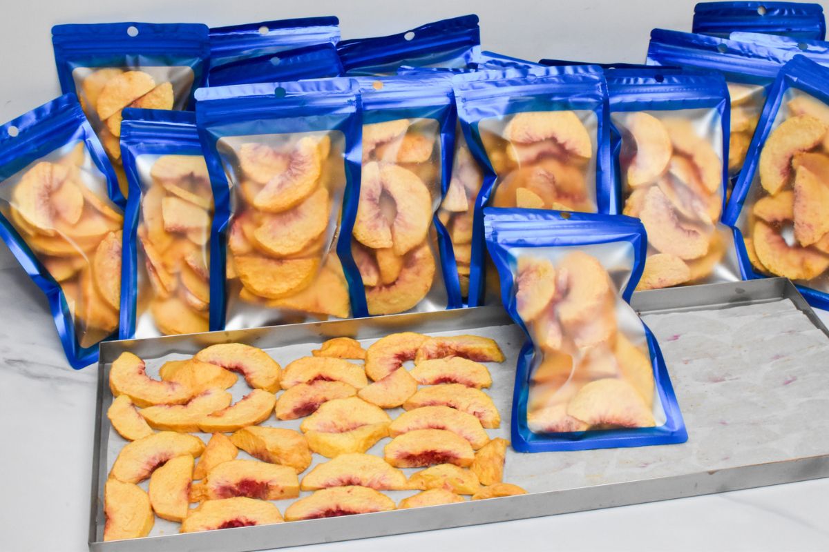 Freeze dried peaches on a metal tray and many bags of freeze dried peaches sealed in mylar bags.