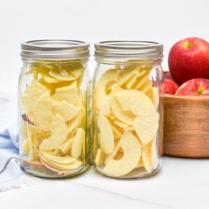 Freeze dried apples in two mason jars and a wooden bowl of apples next to them.