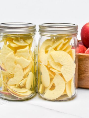 Freeze dried apples in two mason jars and a wooden bowl of apples next to them.
