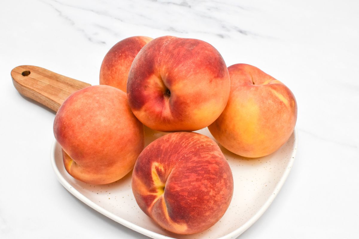 Five peaches on a plate with a wood handle.