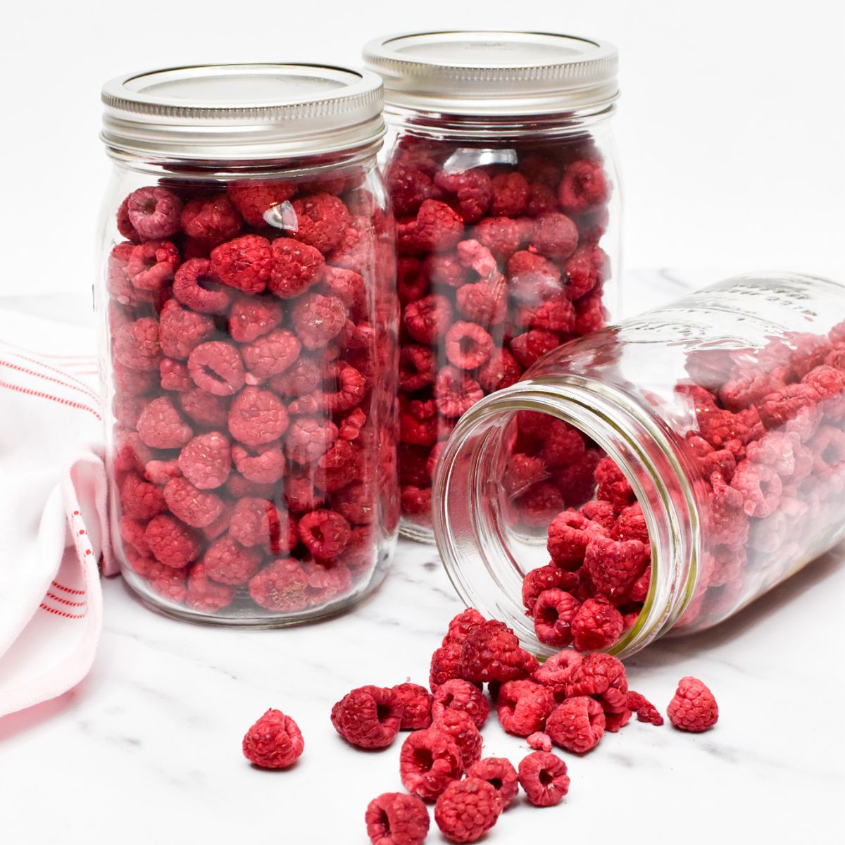 Three jars of freeze dried raspberries with one jar turned on it's side with raspberries spilling out.