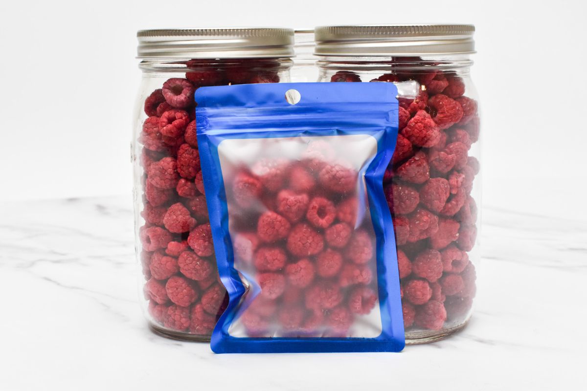 Two jars of freeze dried raspberries with a small Mylar bag of freeze dried raspberries in front of the jars.