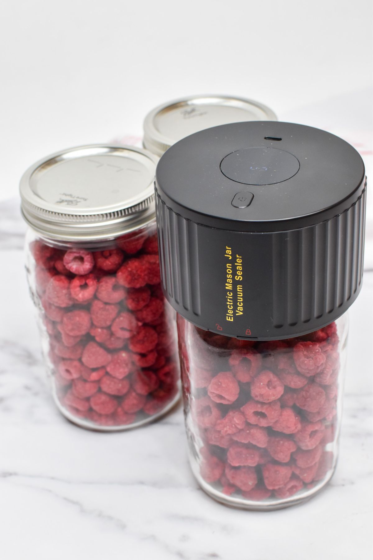 An electric mason jar vacuum sealer on top of a glass jar of freeze dried raspberries.