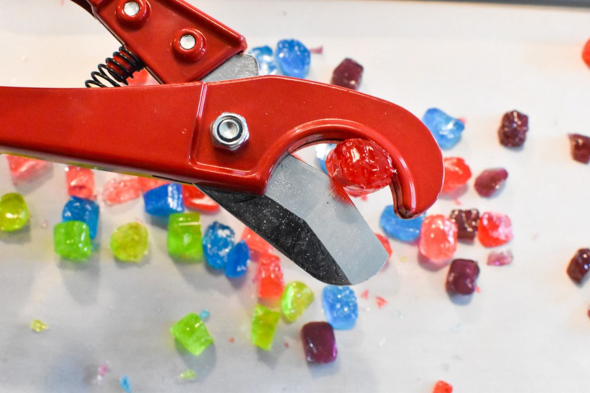 A red pipe cutter being used to cut a red Jolly Rancher into smaller pieces.