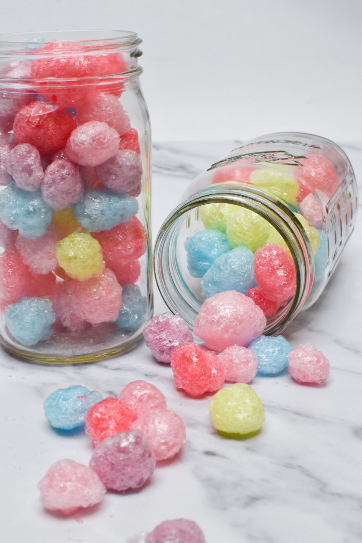 Two glass jars filled with freeze dried Jolly Ranchers, with one jar tipped on its side as candy spills out.