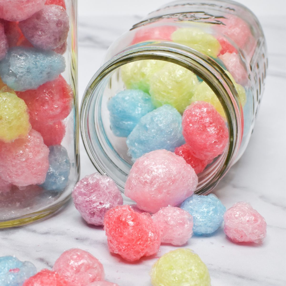 Two glass jars of freeze dried Jolly Ranchers with one turned on its side with freeze dried Jolly Ranchers spilling out.