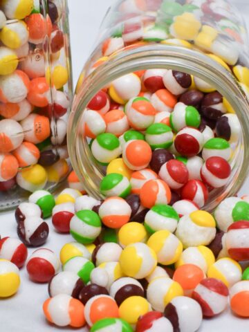 A glass jar with freeze dried Skittles spilling out of it.