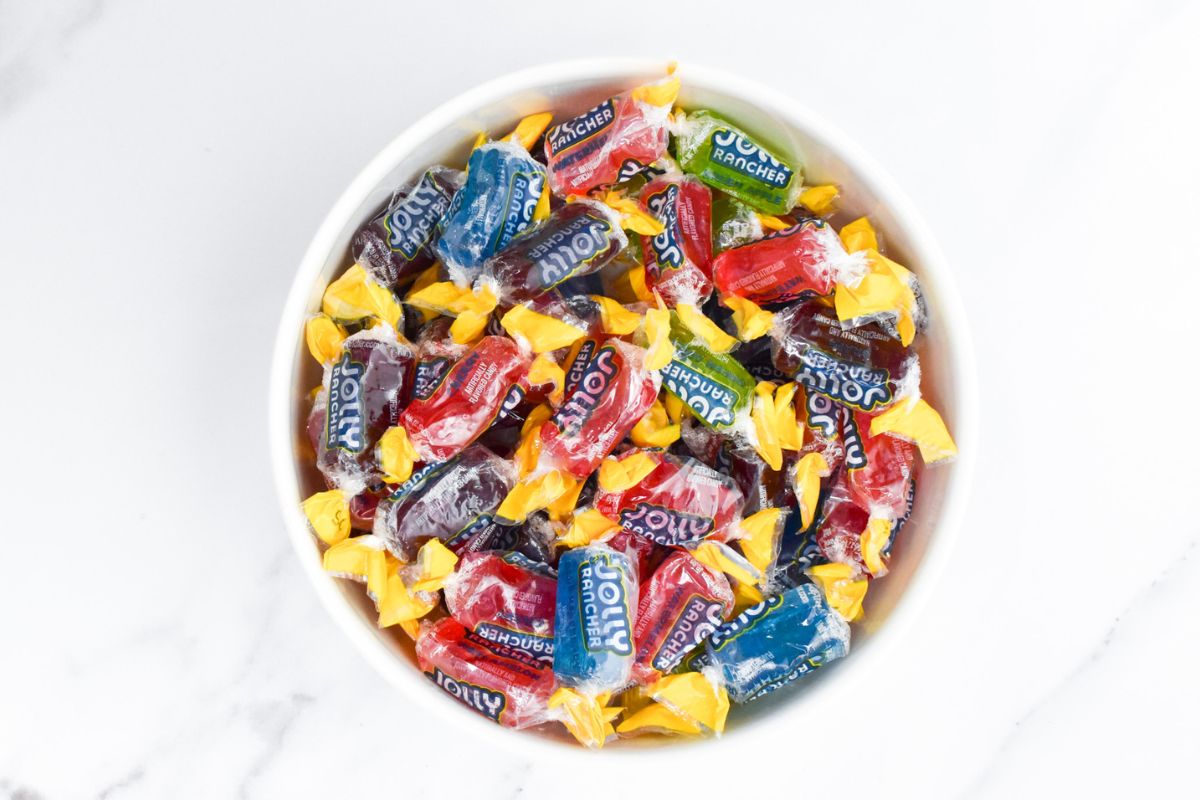 A white bowl full of Jolly Ranchers still wrapped in their wrappers.
