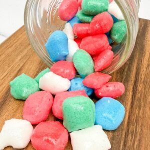 A glass jar turned on its side with freeze dried Airheads spilling out onto a wooden board.