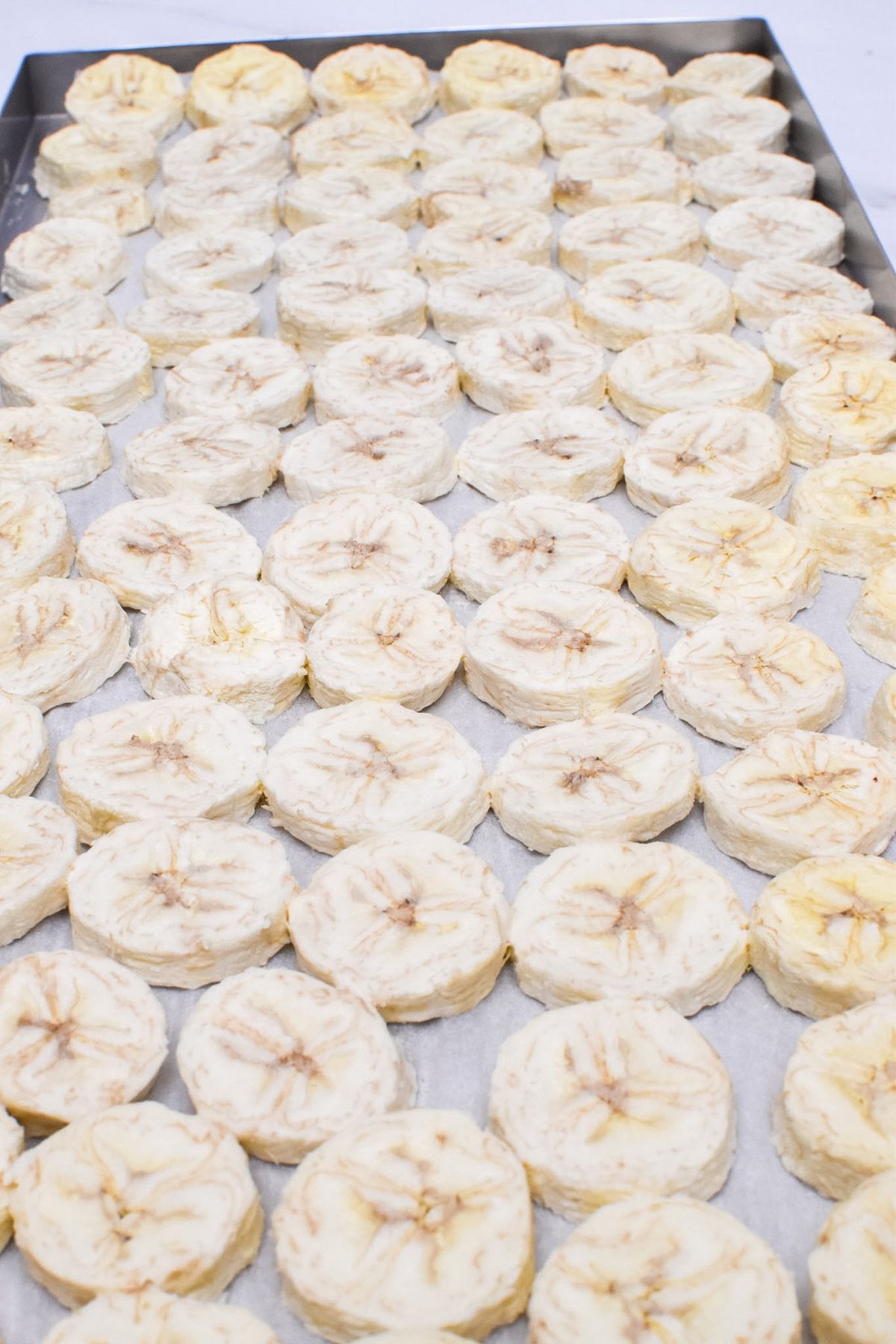 A freeze dryer tray lined with parchment paper with freeze dried bananas on it.