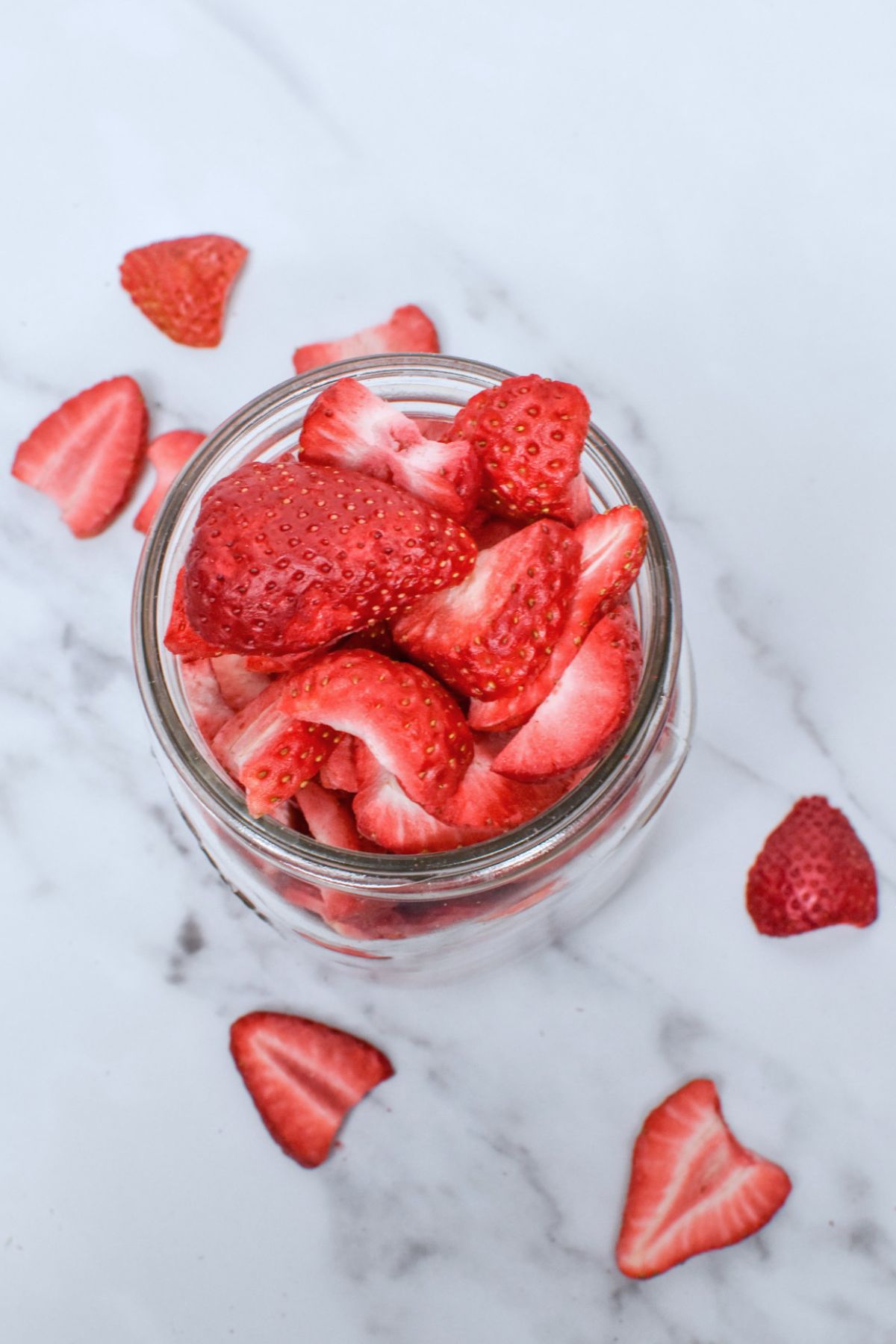 A mason jar filled with freeze dried strawberries and a few sprinkled around it on the counter below.