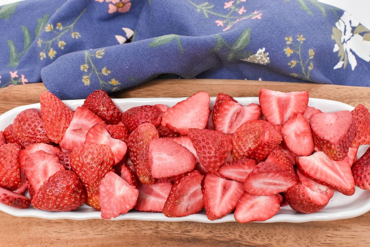 Freeze dried strawberries in a long oval dish on a wooden serving board.