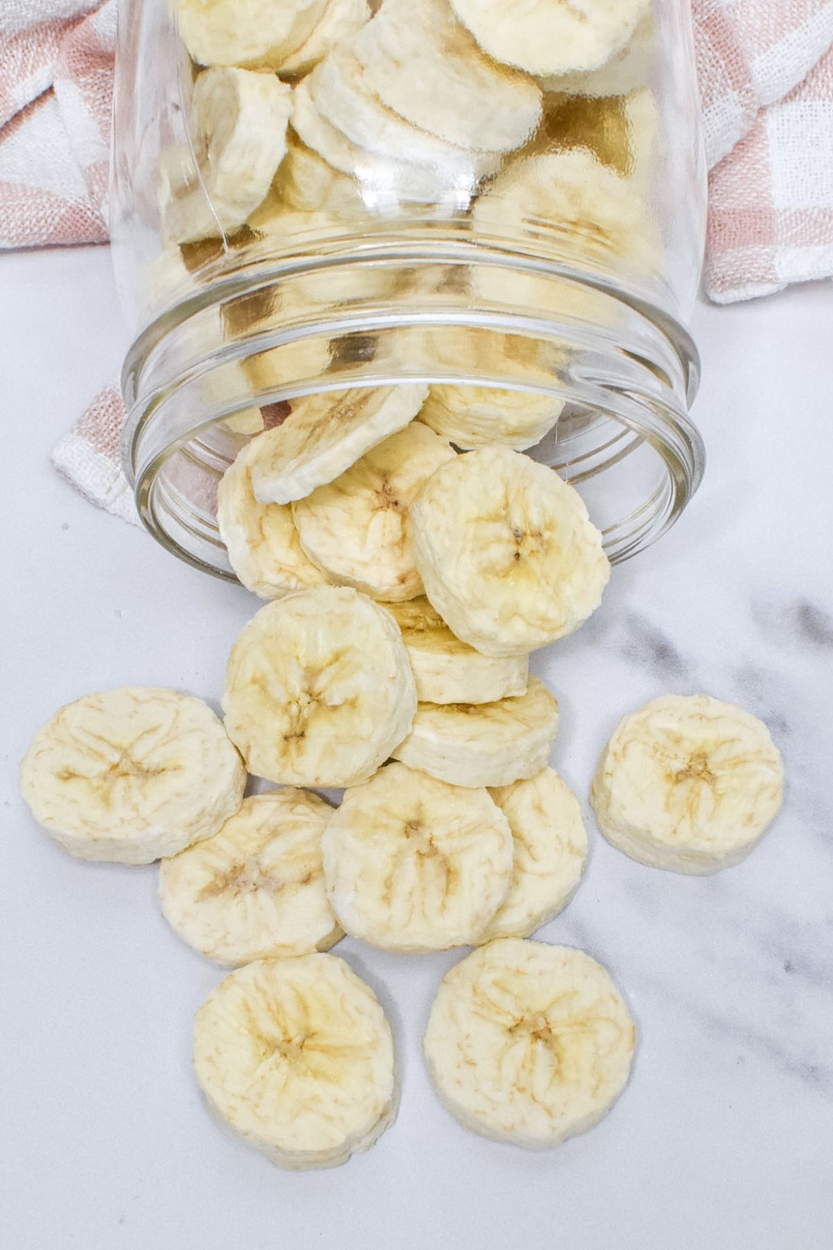 A glass mason jar laying on it's side with freeze dried bananas spilling onto the counter.