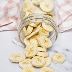 A glass mason jar laying on it's side with freeze dried bananas spilling onto the counter.