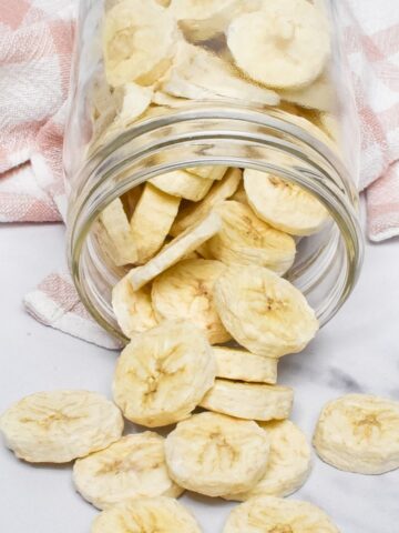 A glass mason jar laying on it's side with freeze dried bananas spilling onto the counter.