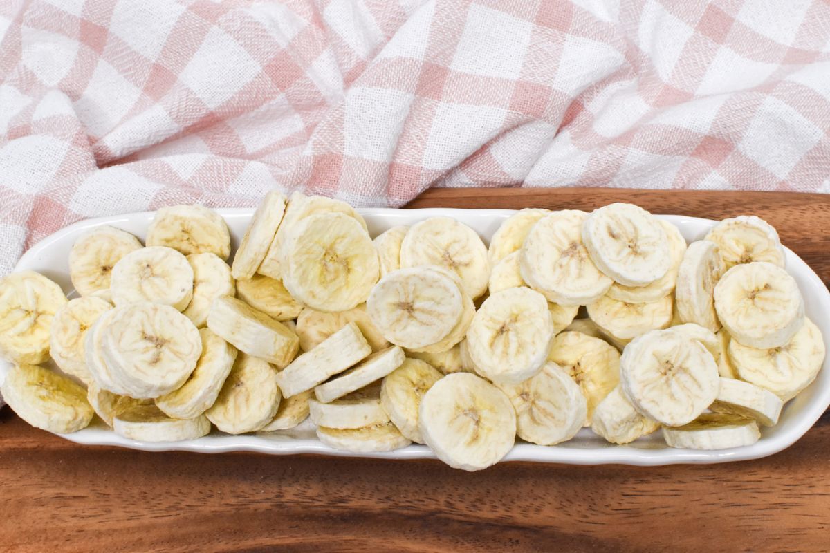 Freeze dried bananas in a long oval dish on a wooden serving board.
