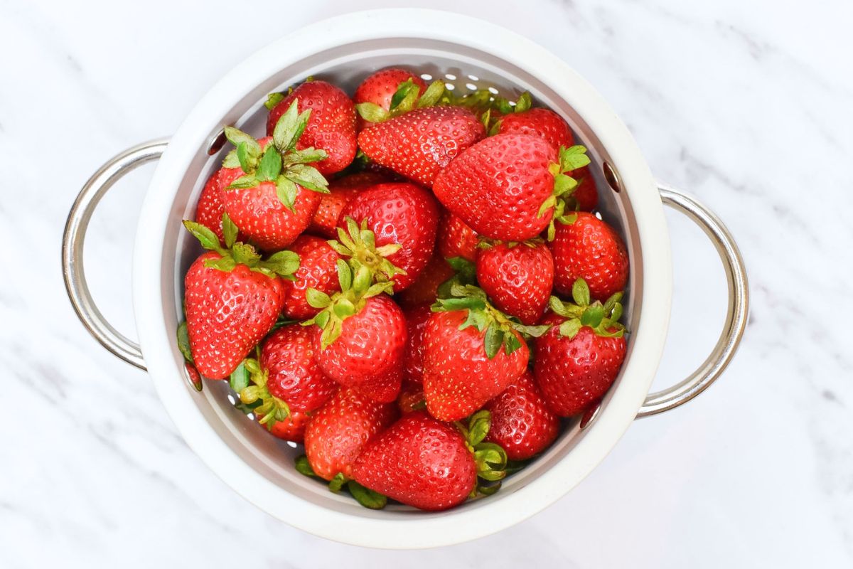 A small white colander filled with fresh strawberries.