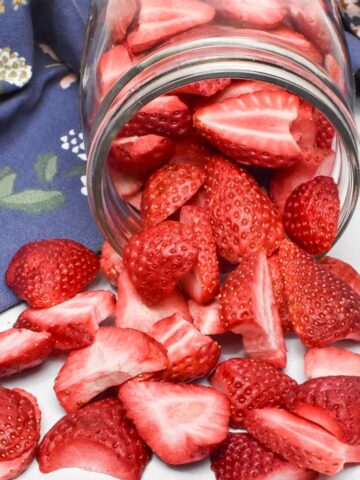 A glass mason jar laying on it's side with freeze dried strawberries spilling onto the counter.