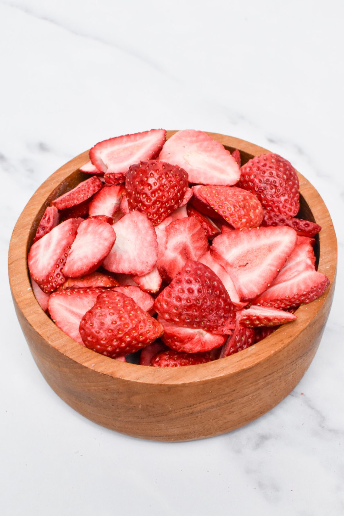 A wooden bowl full of freeze dried strawberries.