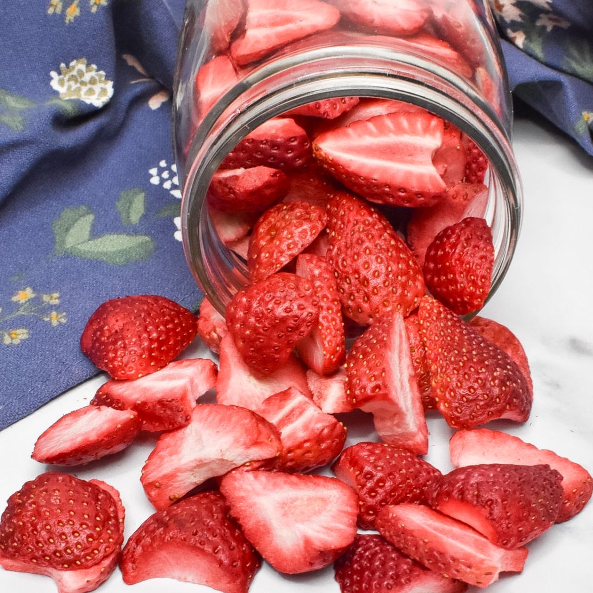 A glass mason jar laying on it's side with freeze dried strawberries spilling onto the counter.