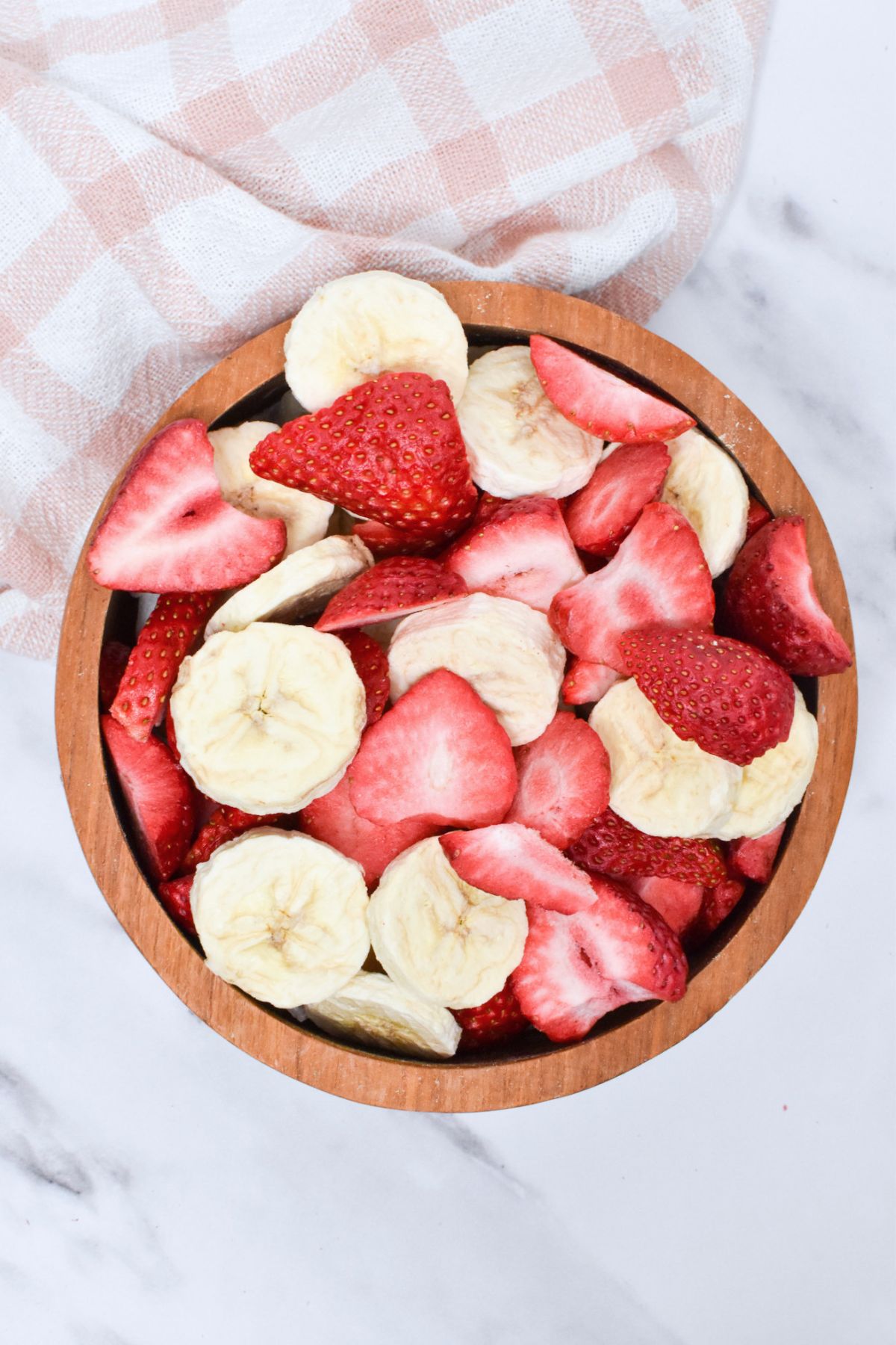 A wooden bowl full of freeze dried bananas and strawberries.
